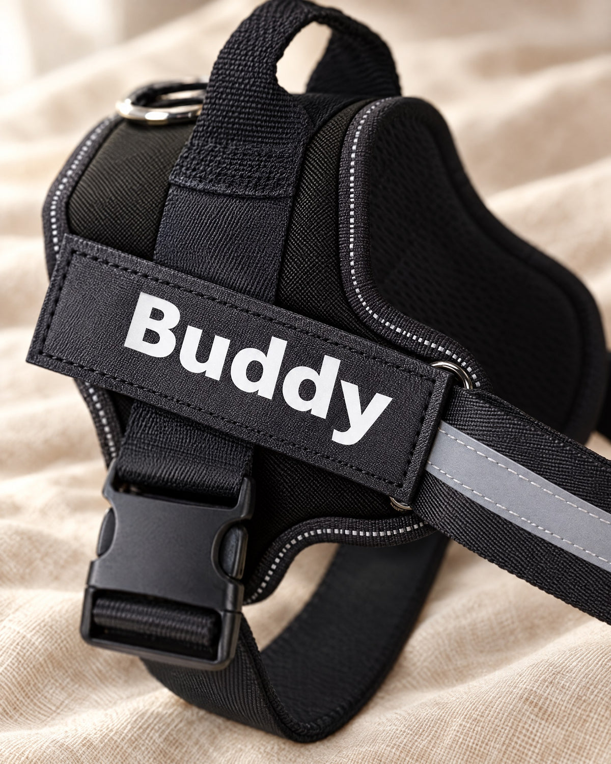 Close-up of the black Fleecy harness showing the printed name patch, stitching, buckle and reflective strip